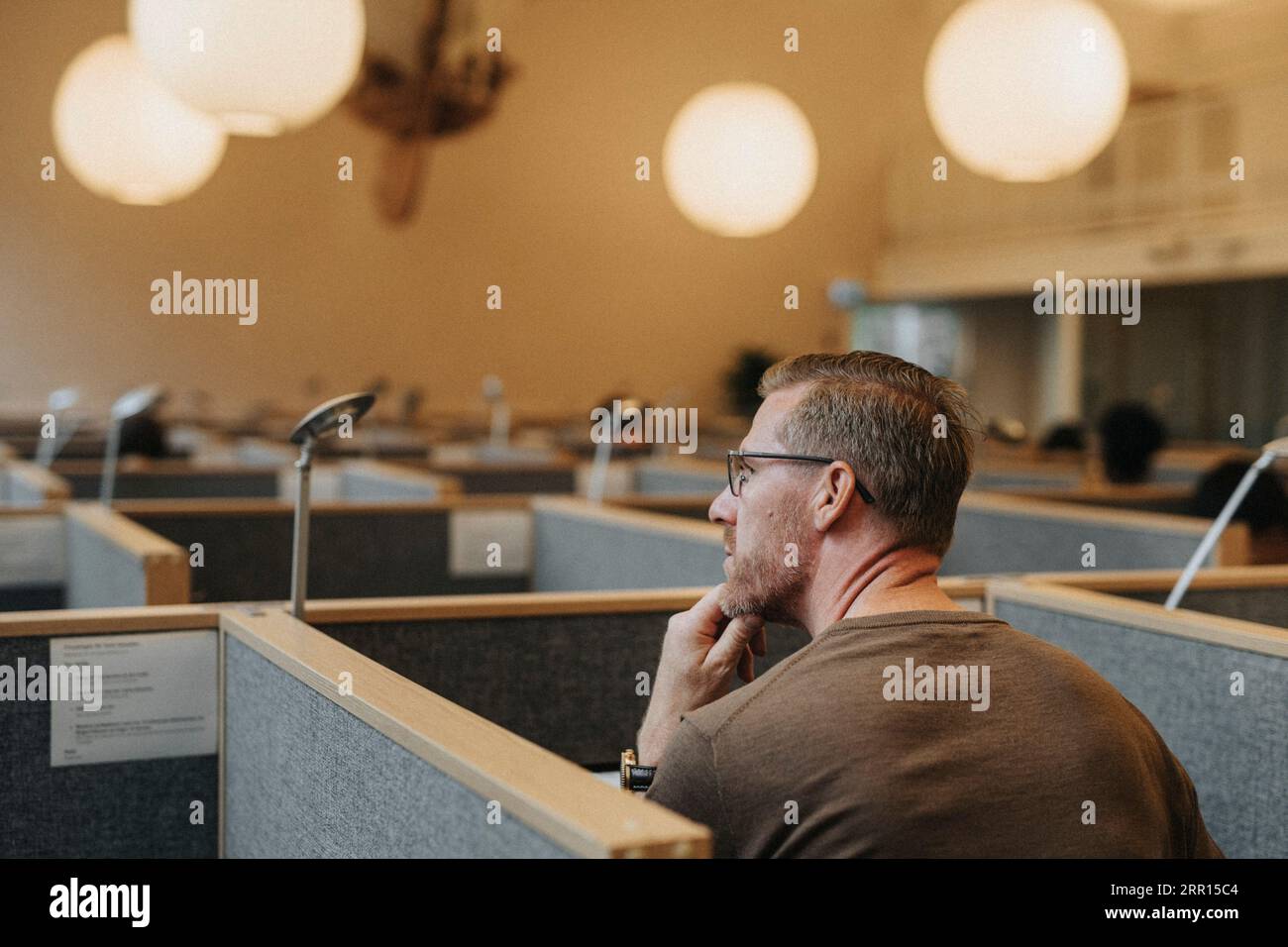 Rückansicht eines nachdenklichen männlichen Professors, der in der Bibliothek der Universität sitzt Stockfoto