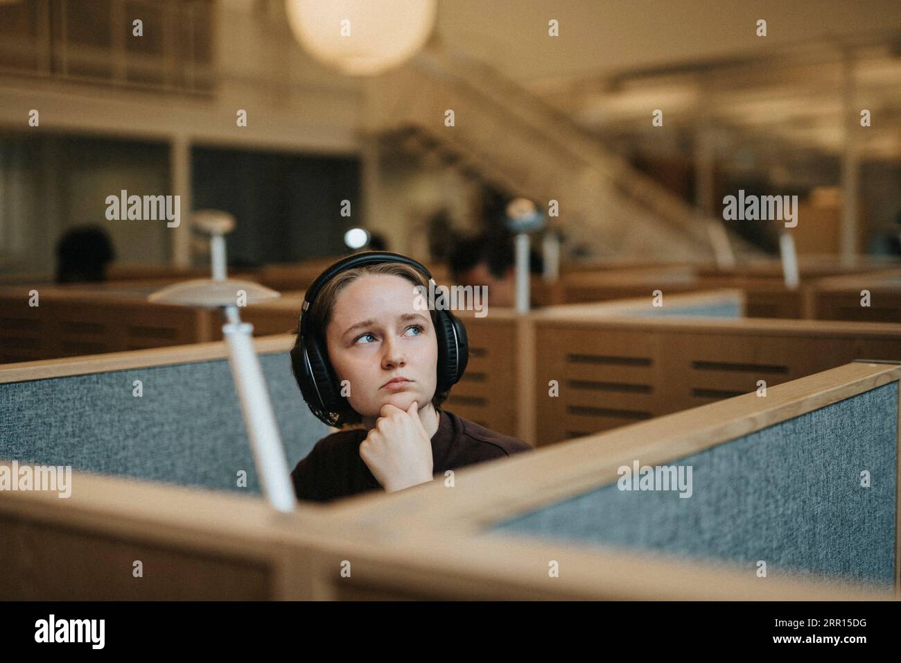 Nachdenklicher junger Student, der mit der Hand auf dem Kinn in der Universitätsbibliothek sitzt Stockfoto