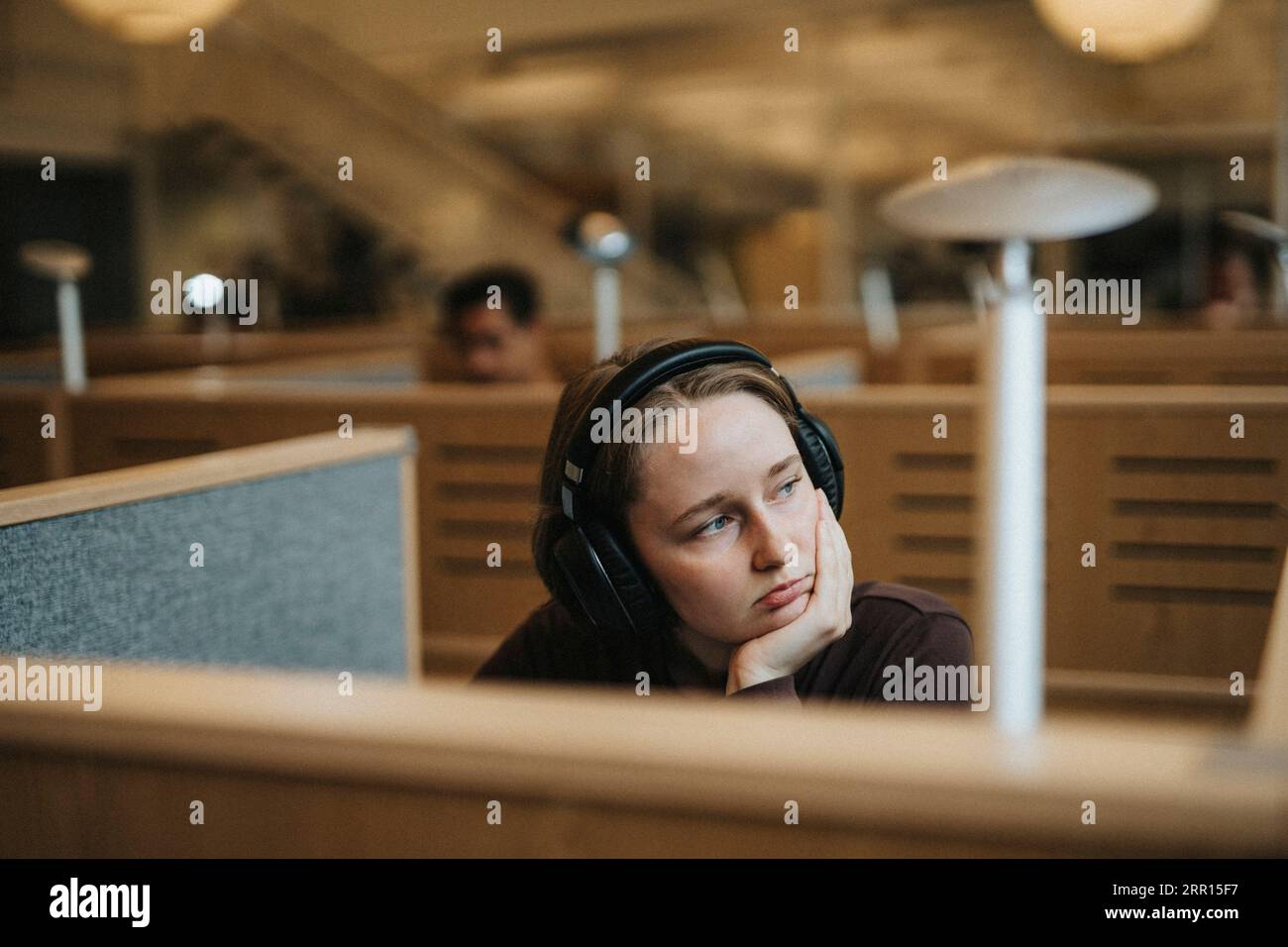 Kontemplative junge Studentin mit der Hand am Kinn in der Universitätsbibliothek Stockfoto