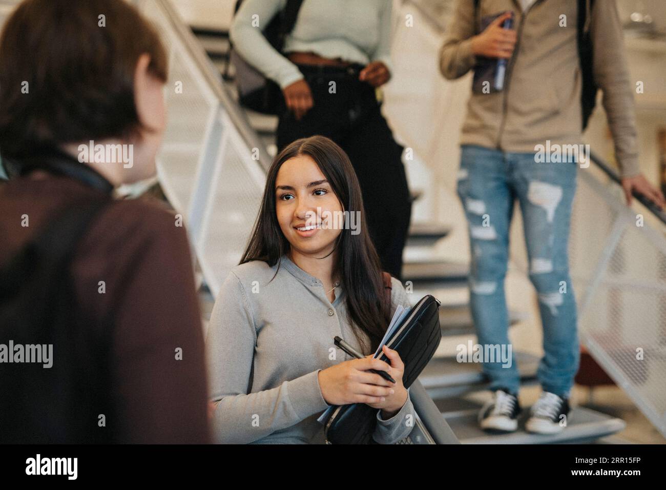 Lächelnde Studentin, die mit einem Freund diskutiert, während sie an der Treppe in der Universität steht Stockfoto