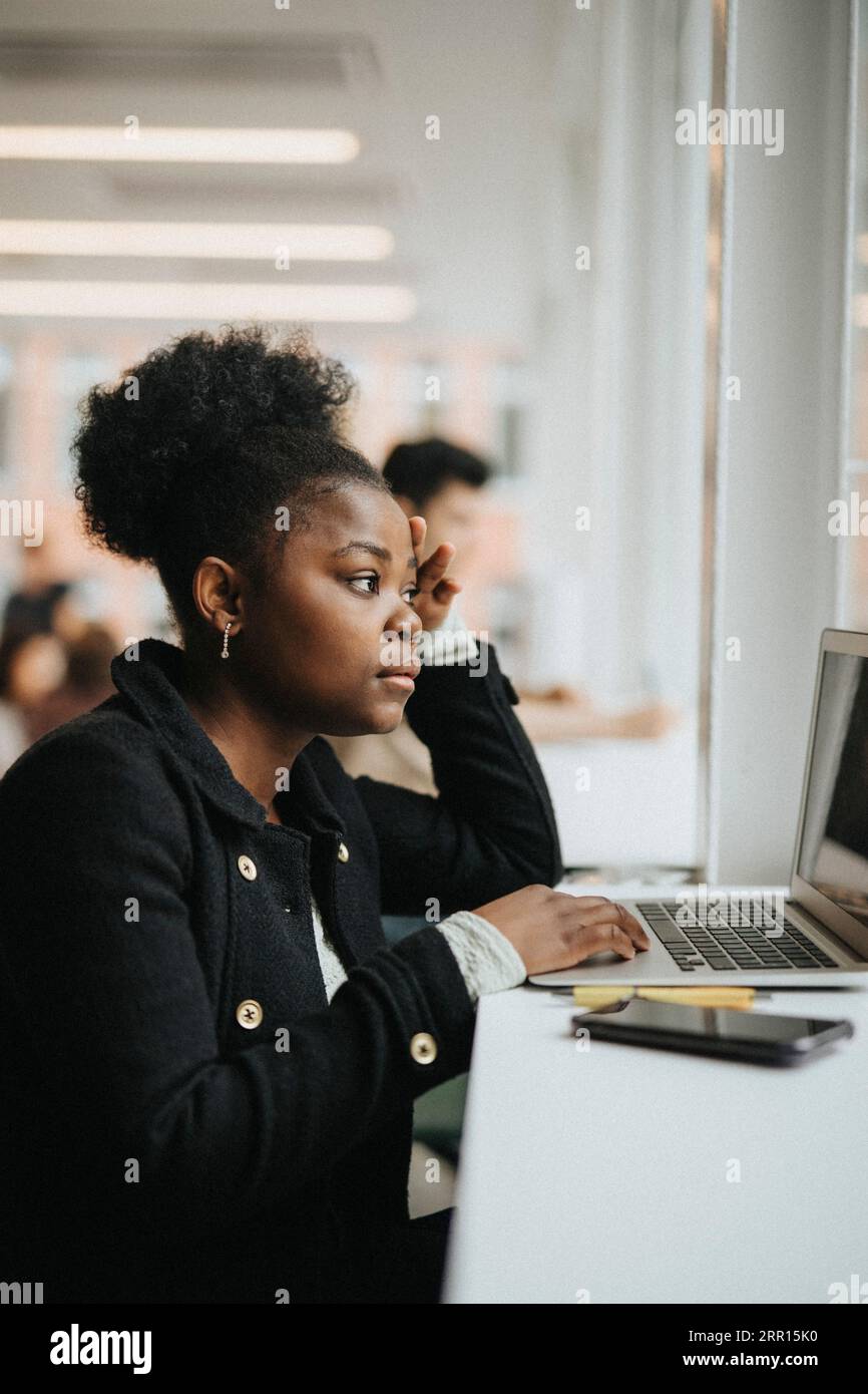 Ernsthafte Studentin, die an der Universität auf Laptop studiert Stockfoto
