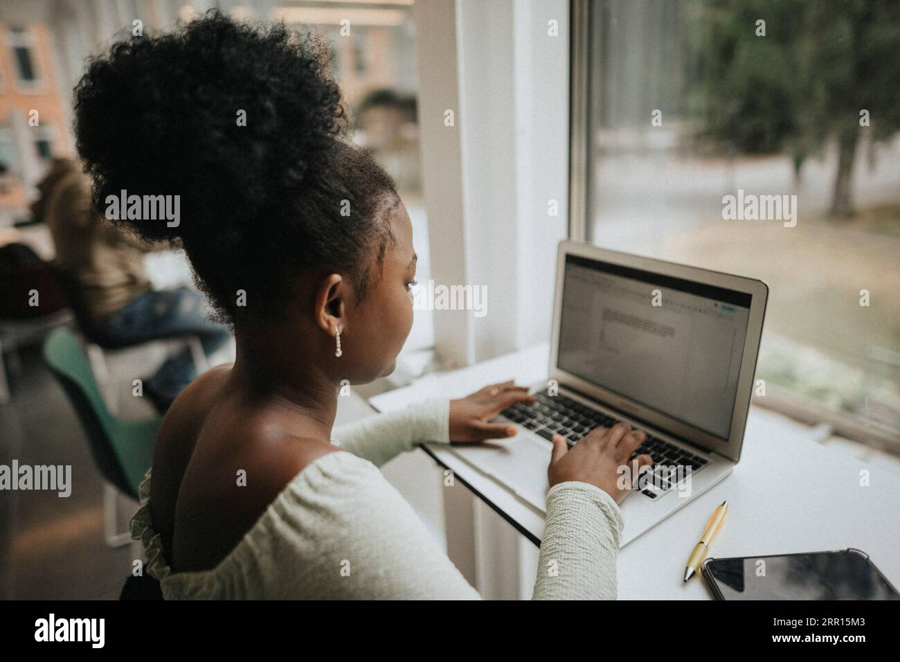 Seitenansicht einer Studentin mit Laptop am Tisch der Universität Stockfoto