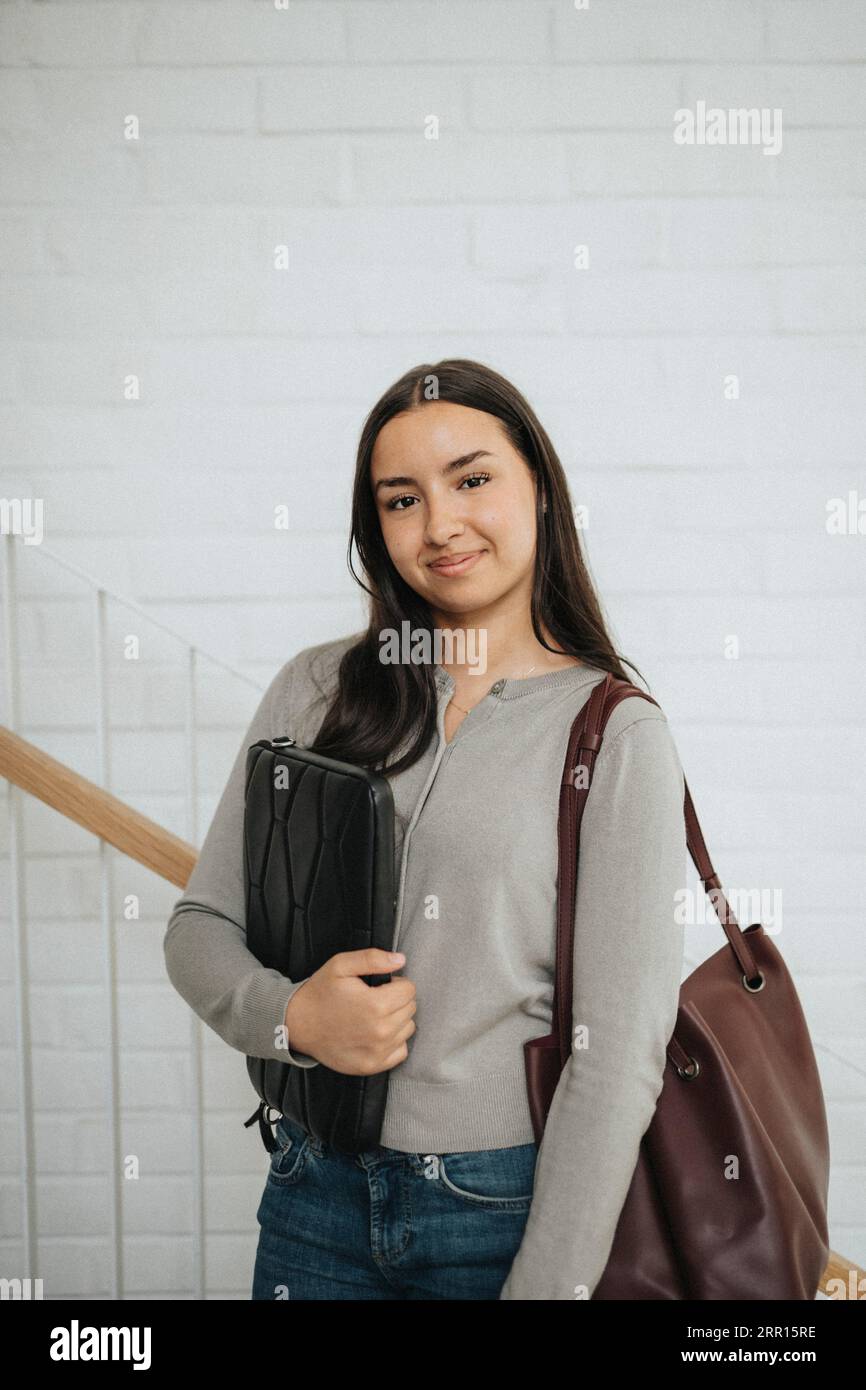 Porträt einer selbstbewussten Studentin mit an der Wand stehender Mappe an der Universität Stockfoto