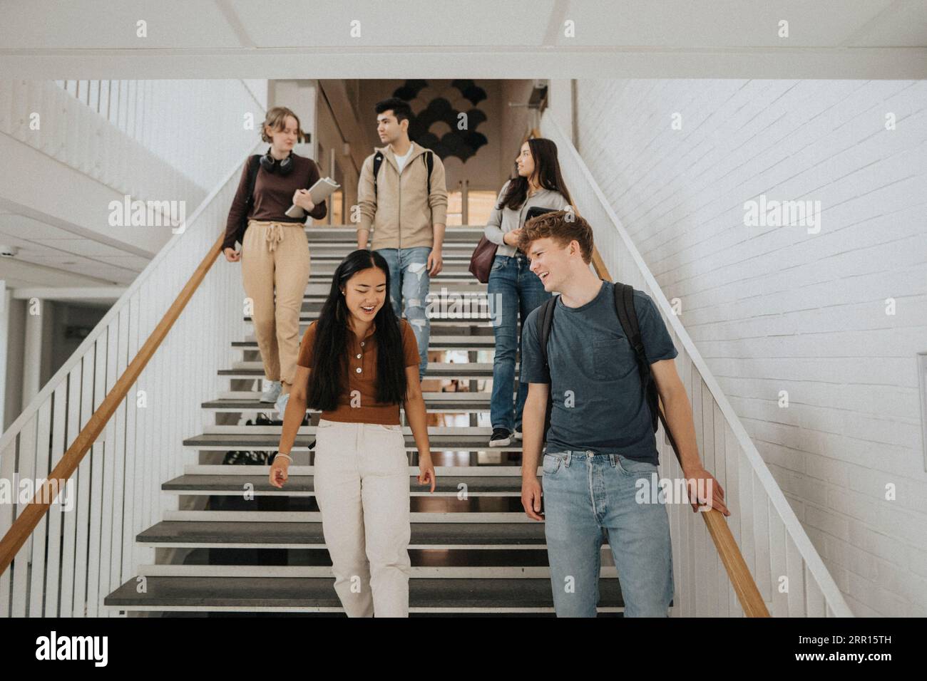 Glückliche multirassische männliche und weibliche Studenten, die auf Stufen in der Universität gehen Stockfoto