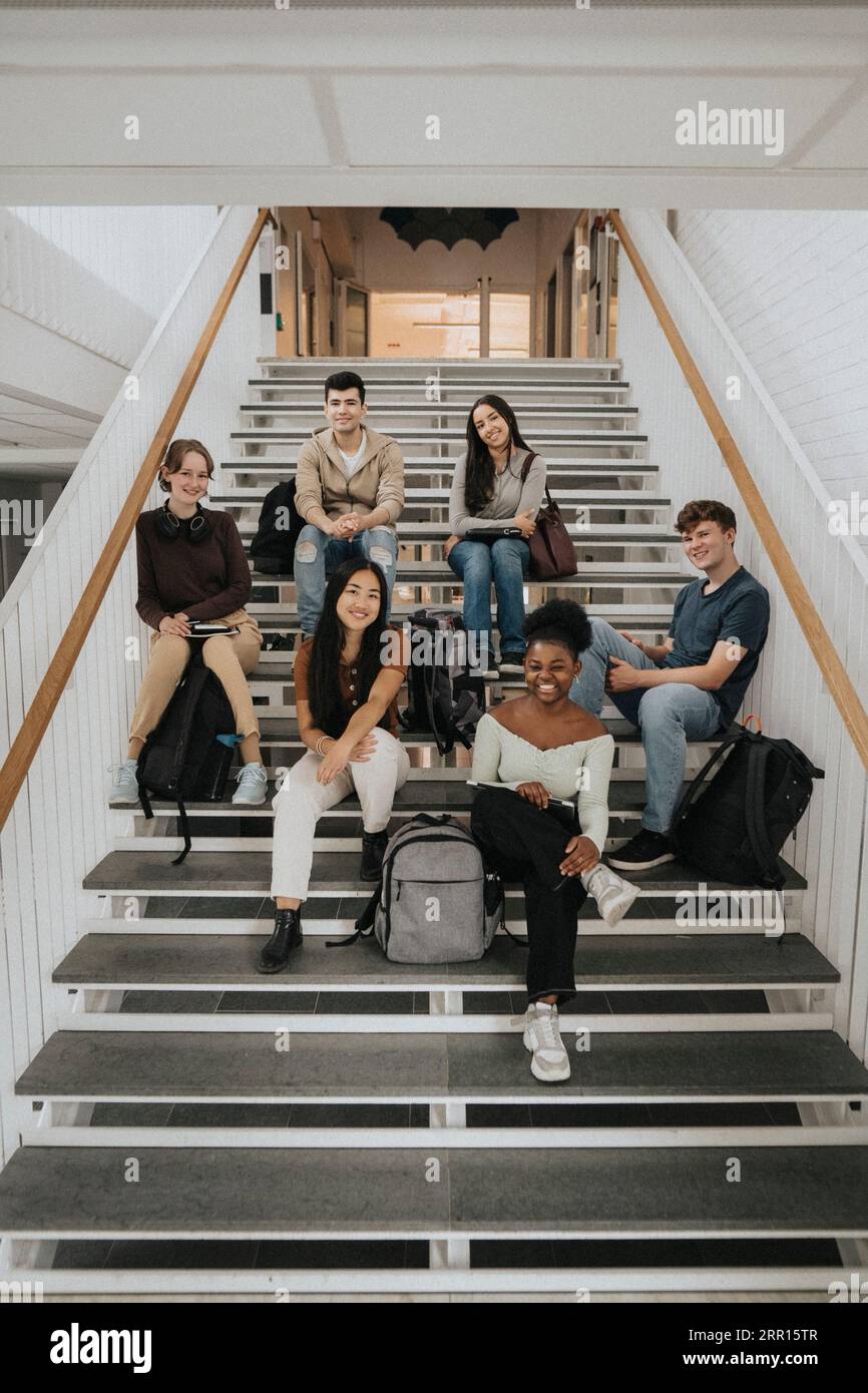 Fröhliche, multirassische Studenten, die an der Universität auf Treppen sitzen Stockfoto
