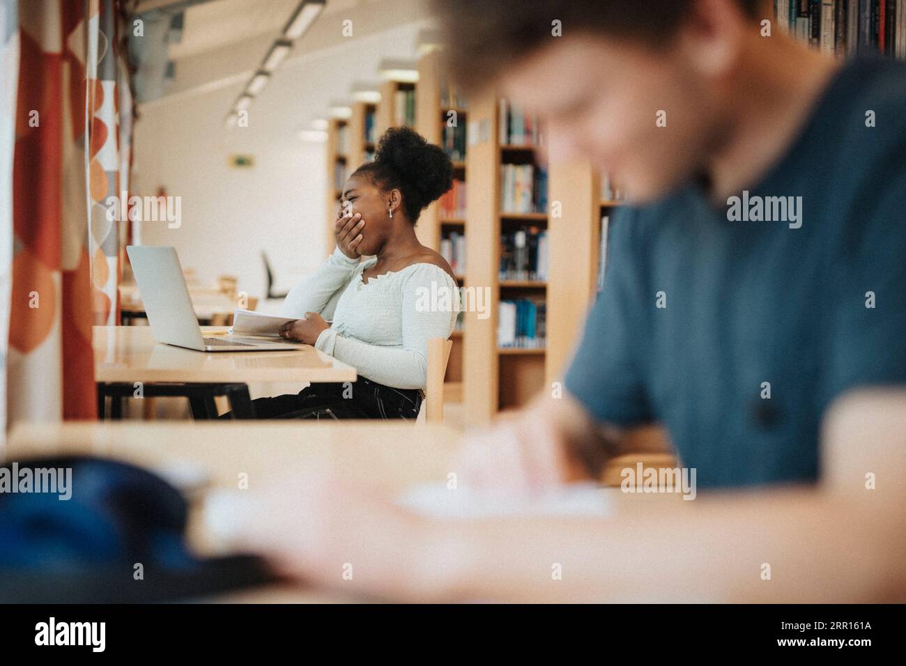 Student Gähnen während des Studiums in der Bibliothek an der Universität Stockfoto