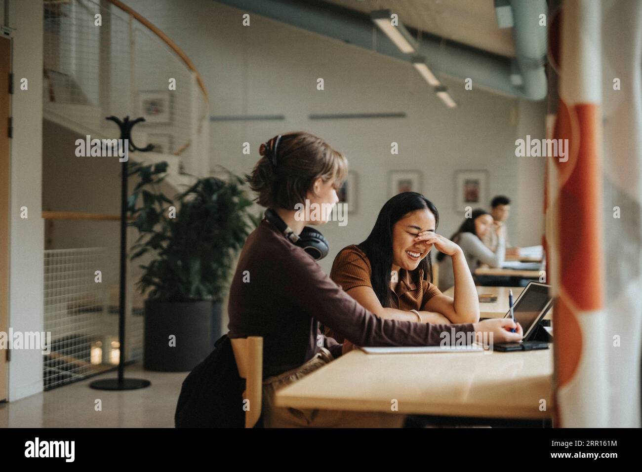 Schüler lächelt beim Lernen mit Freund am Tisch in der Bibliothek Stockfoto
