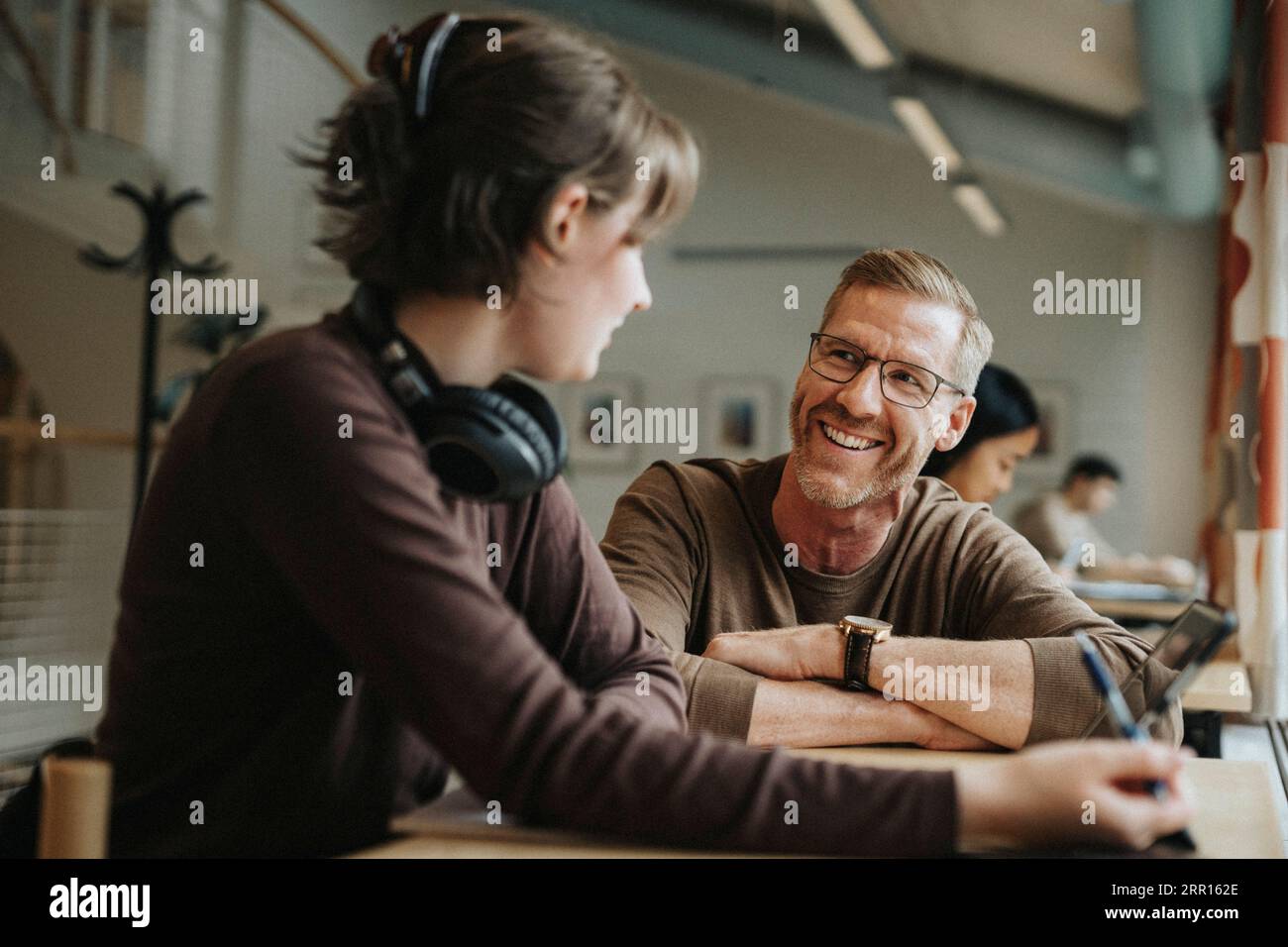 Glücklicher Professor, der mit Studenten in der Bibliothek an der Universität diskutiert Stockfoto