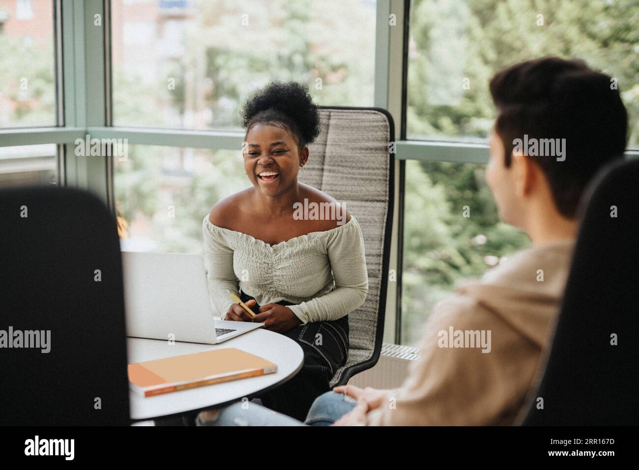 Fröhlicher Student mit Laptop am Tisch in der Universität Stockfoto