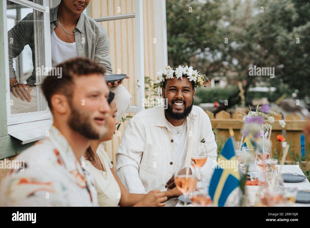 Porträt eines glücklichen jungen Mannes, der eine Diadem trägt, während er mit Freunden während einer Dinnerparty im Café sitzt Stockfoto