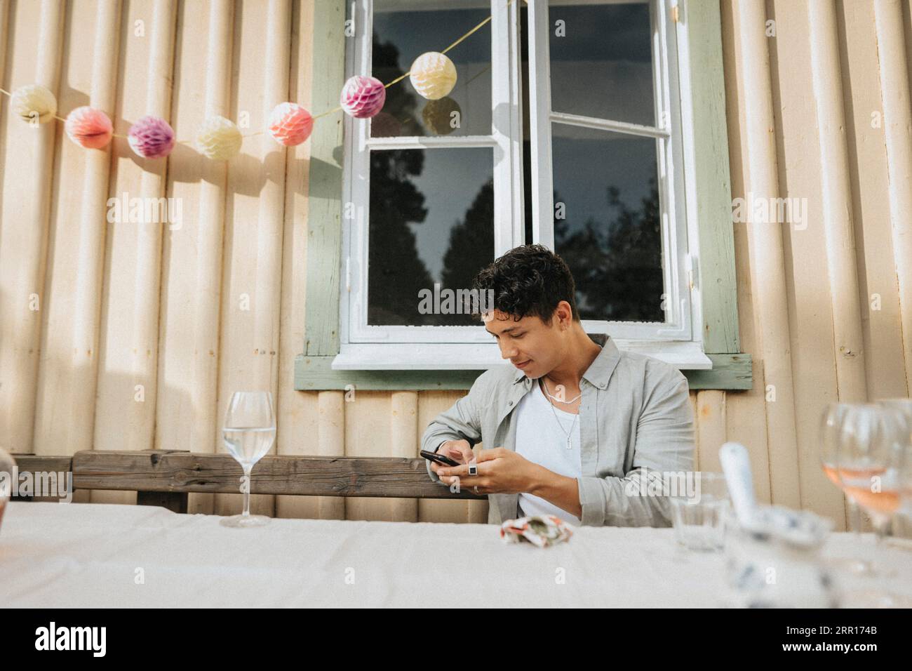 Junger Mann, der während der Dinnerparty am Tisch sitzt und das Smartphone benutzt Stockfoto