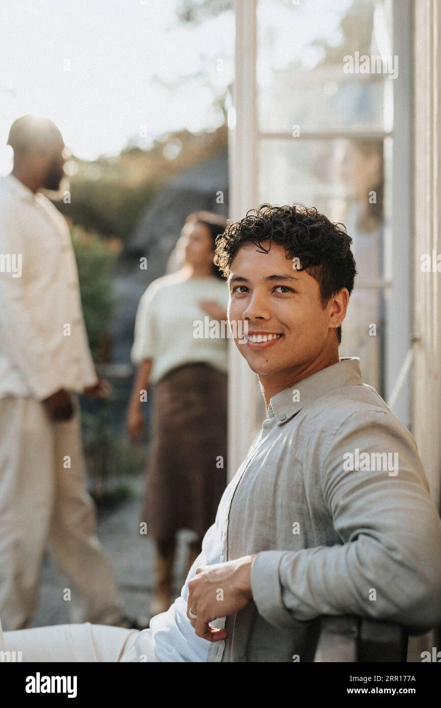 Seitenansicht des lächelnden jungen Mannes während der Dinnerparty im Café Stockfoto