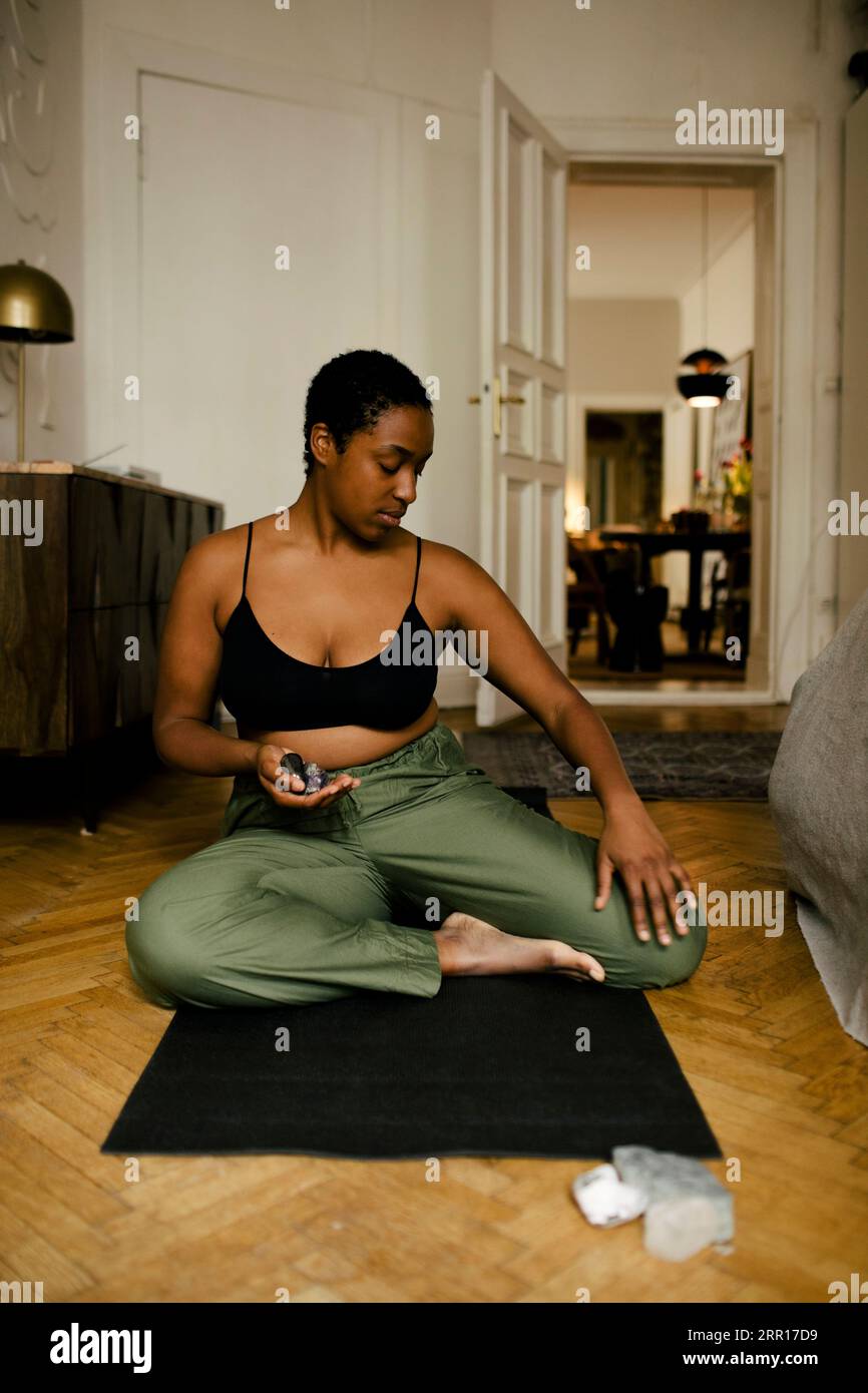 Junge Frau, die Steine hält, während sie zu Hause Entspannungsübungen durchführt Stockfoto
