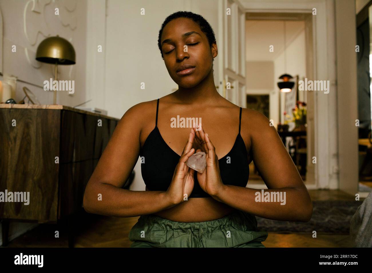 Junge Frau, die Stein hält, während sie zu Hause meditiert Stockfoto