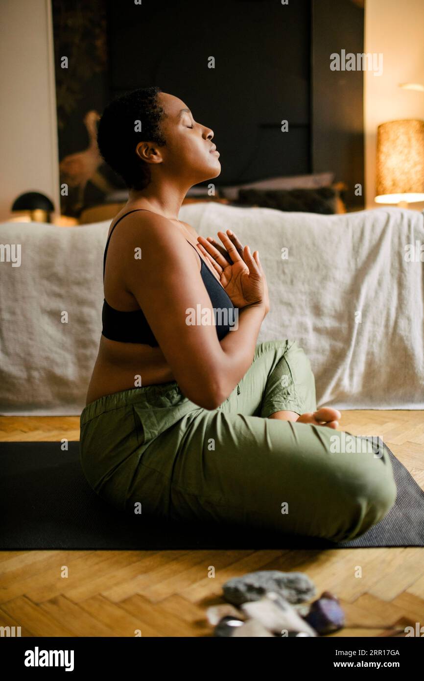 Seitenansicht einer jungen Frau, die im Schlafzimmer zu Hause meditiert Stockfoto