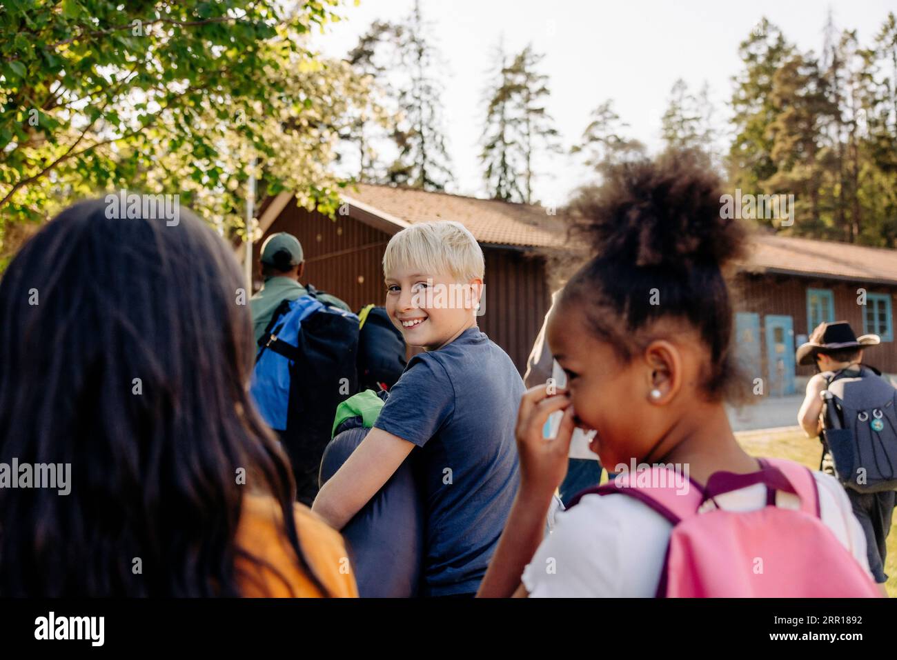 Porträt eines lächelnden Jungen, der über die Schulter schaut, während er mit Freunden im Sommercamp spaziert Stockfoto