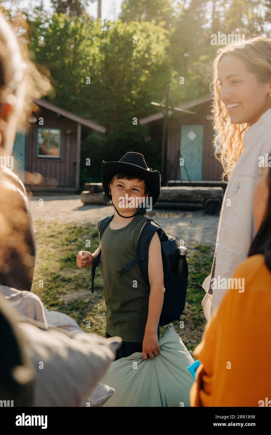 Junge mit Hut und Rucksack, der mit Freunden im Sommercamp steht Stockfoto