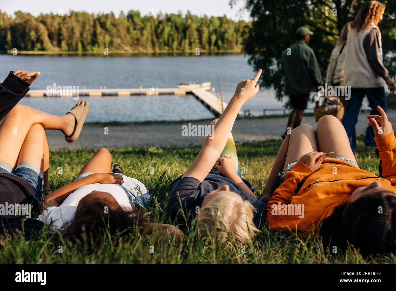 Junge zeigt, während er sich mit Freunden auf dem Rasen im Sommercamp hinlegt Stockfoto