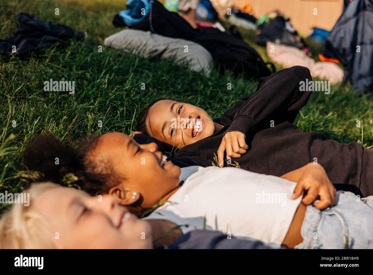 Glückliches Mädchen, das mit Freunden genießt, während es im Sommercamp auf dem Rasen liegt Stockfoto