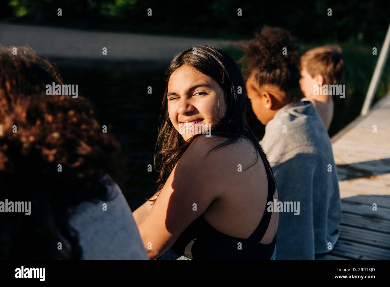 Seitenansicht des Porträts eines lächelnden Mädchens, das mit Freunden auf dem Steg in der Nähe des Sees sitzt Stockfoto