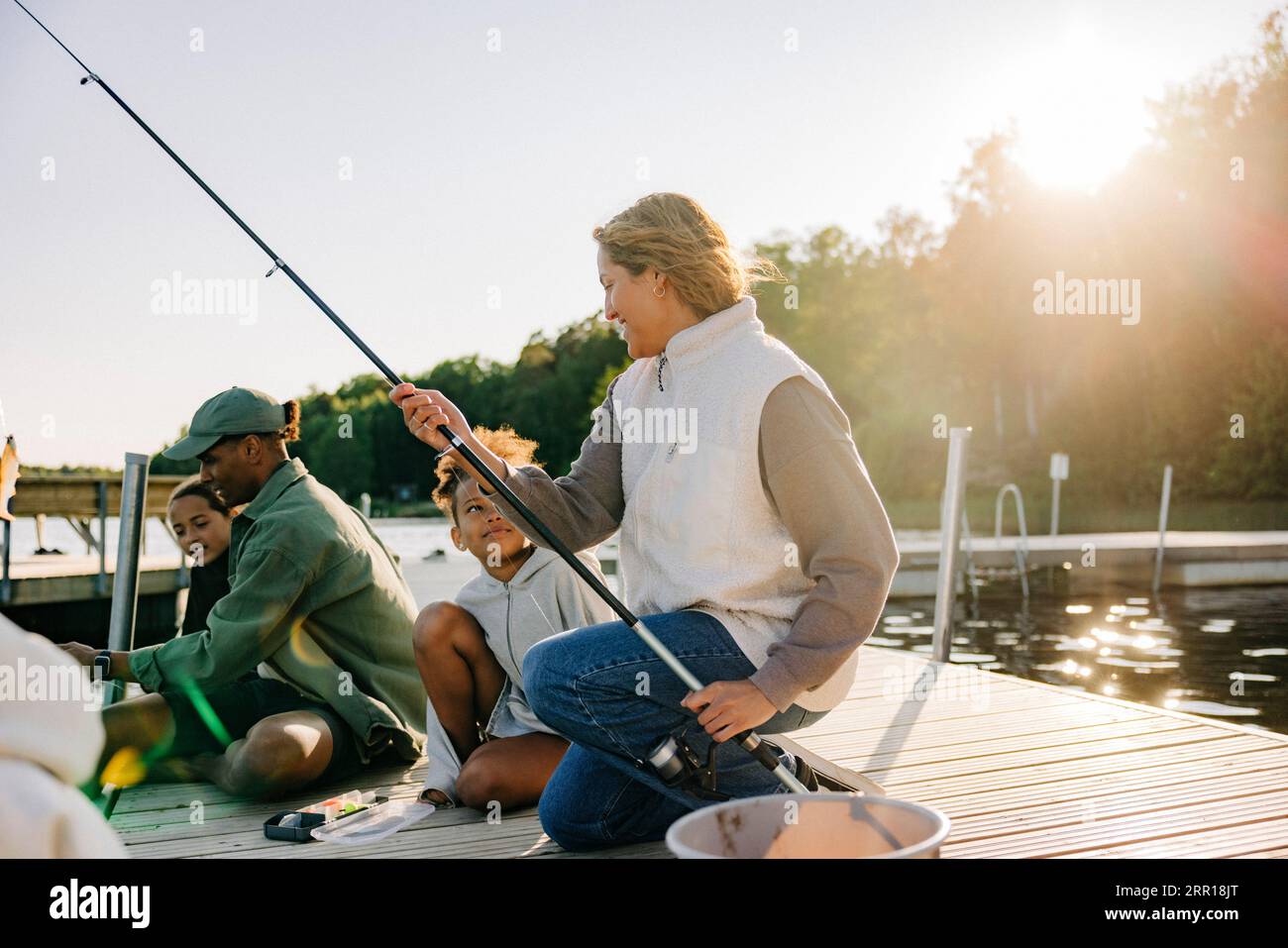 Ratgeber, die Kindern das Angeln lehren, während sie im Sommercamp auf dem Steg in der Nähe des Sees sitzen Stockfoto