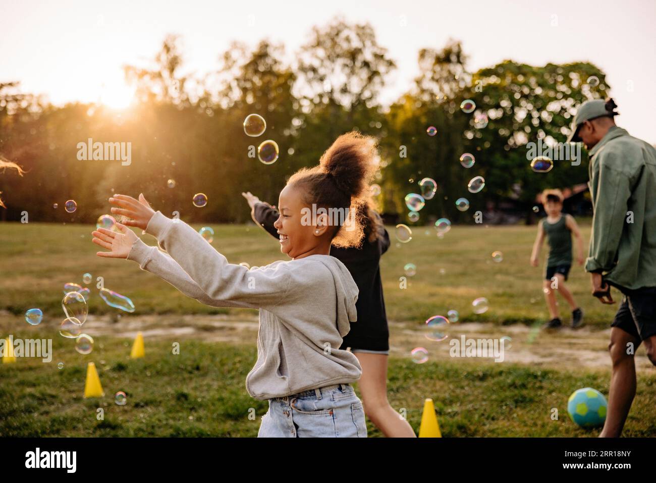 Seitenansicht des glücklichen Mädchens, das beim Spielen mit Freunden auf dem Spielplatz im Sommercamp Blasen fängt Stockfoto