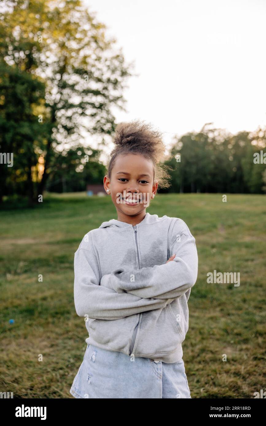 Porträt eines lächelnden Mädchens, das mit gekreuzten Armen auf dem Spielplatz steht Stockfoto