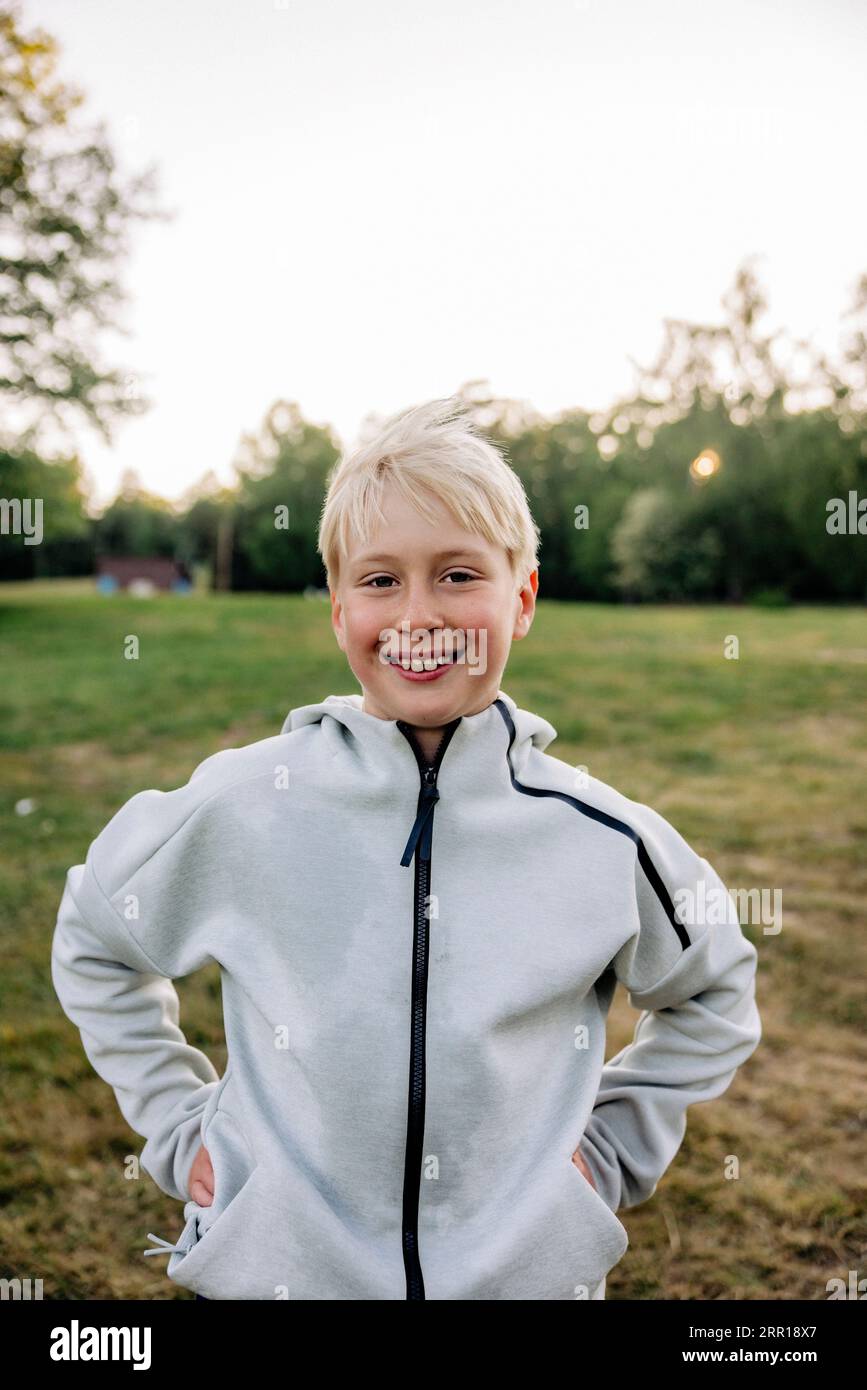 Porträt des lächelnden Jungen, der mit den Händen in den Taschen auf dem Spielplatz steht Stockfoto