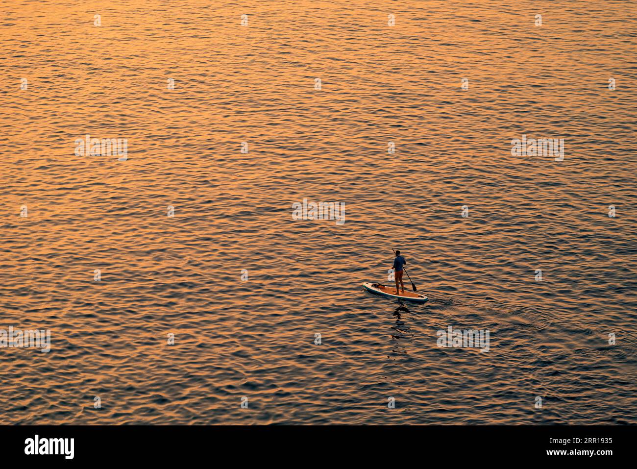 Abenteuerlustige Personen auf einem Stand-Up-Paddle-Board paddeln während eines hellen und lebendigen Sonnenaufgangs Stockfoto