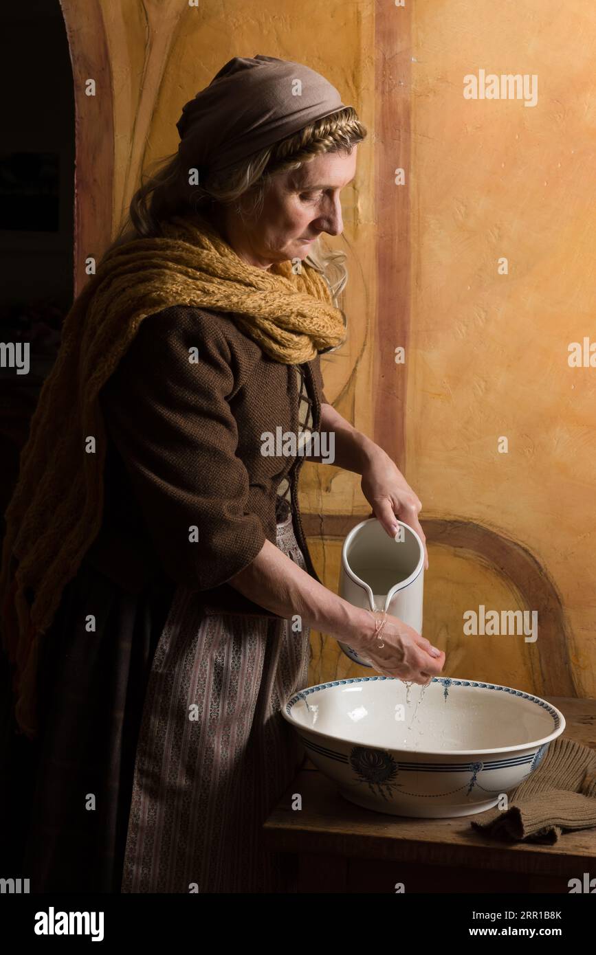 Eine Frau im Bauernrenaissance-Kostüm wäscht sich die Hände in einem antiken Becken Stockfoto