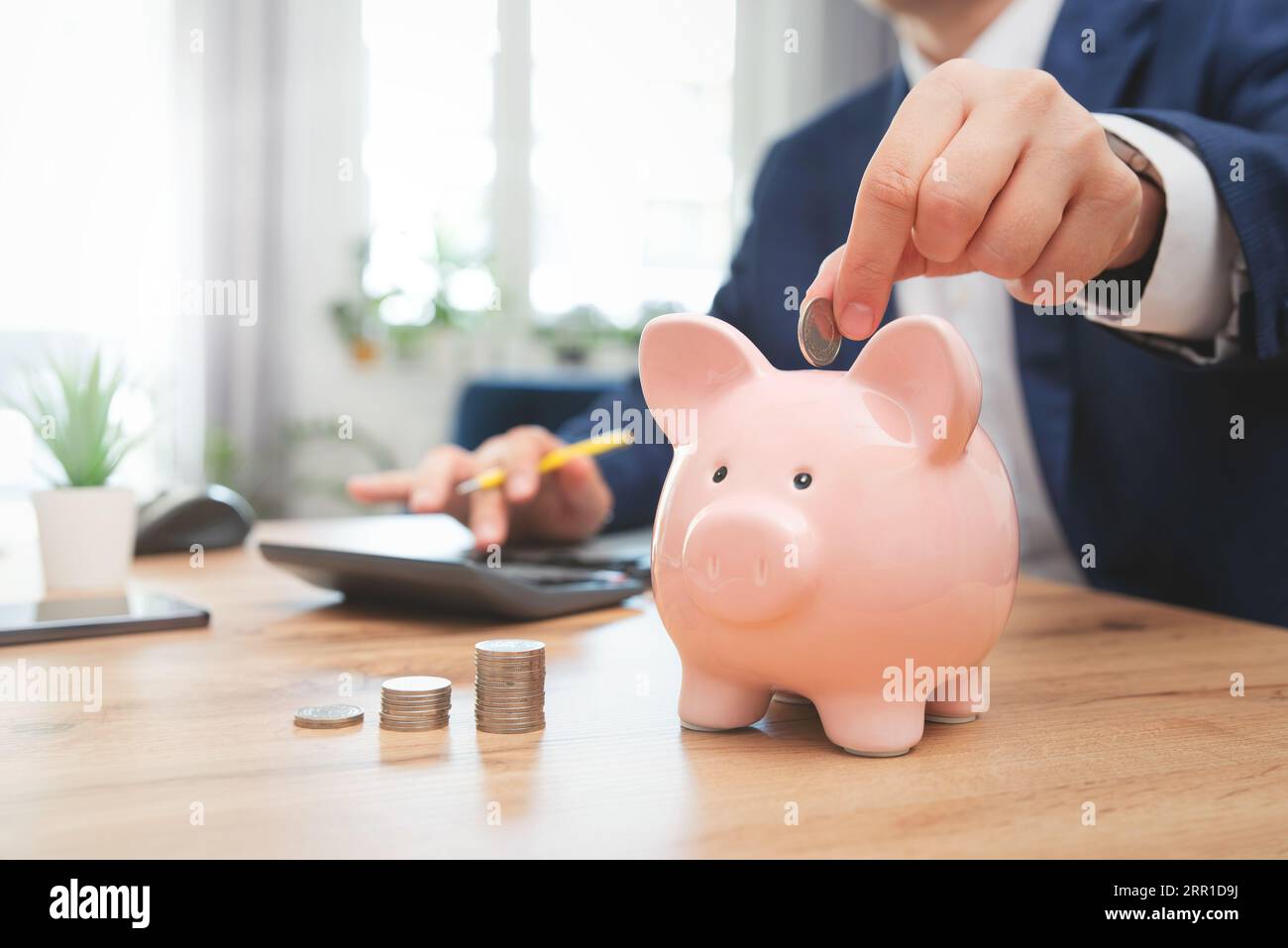 Eine Münze in eine Schweinebank stecken. Einsparungen, Finanzen, Wirtschaft und Haushalt Stockfoto