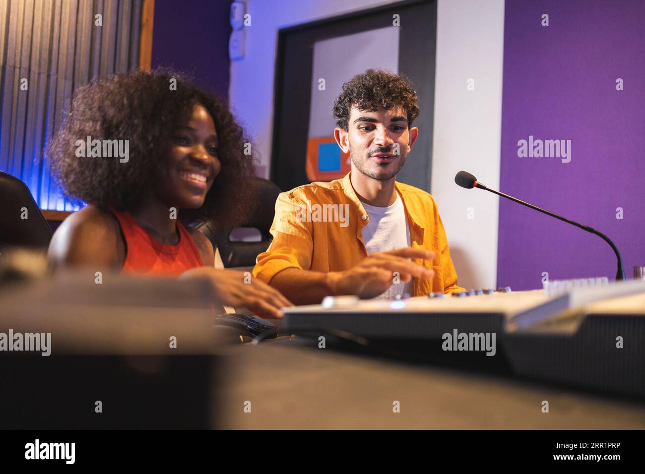 Männliche Toningenieurin und optimistische afroamerikanische Sängerin, die Hit-Songs kreiert, während sie Mischpulte und Computersoftware im Musikstudio verwendet Stockfoto