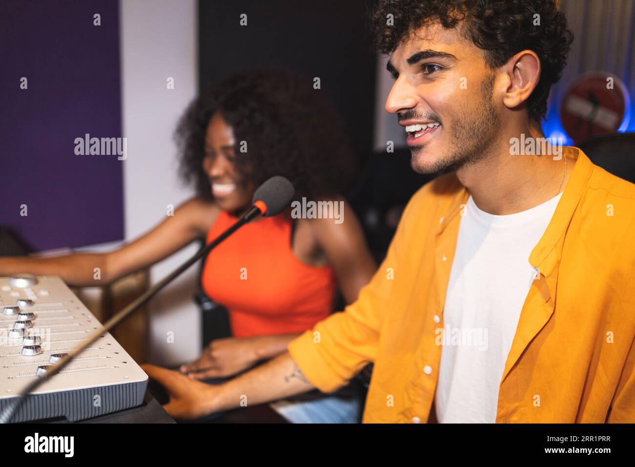 Männliche Toningenieurin und optimistische afroamerikanische Sängerin, die Hit-Songs kreiert, während sie Mischpulte und Computersoftware im Musikstudio verwendet Stockfoto