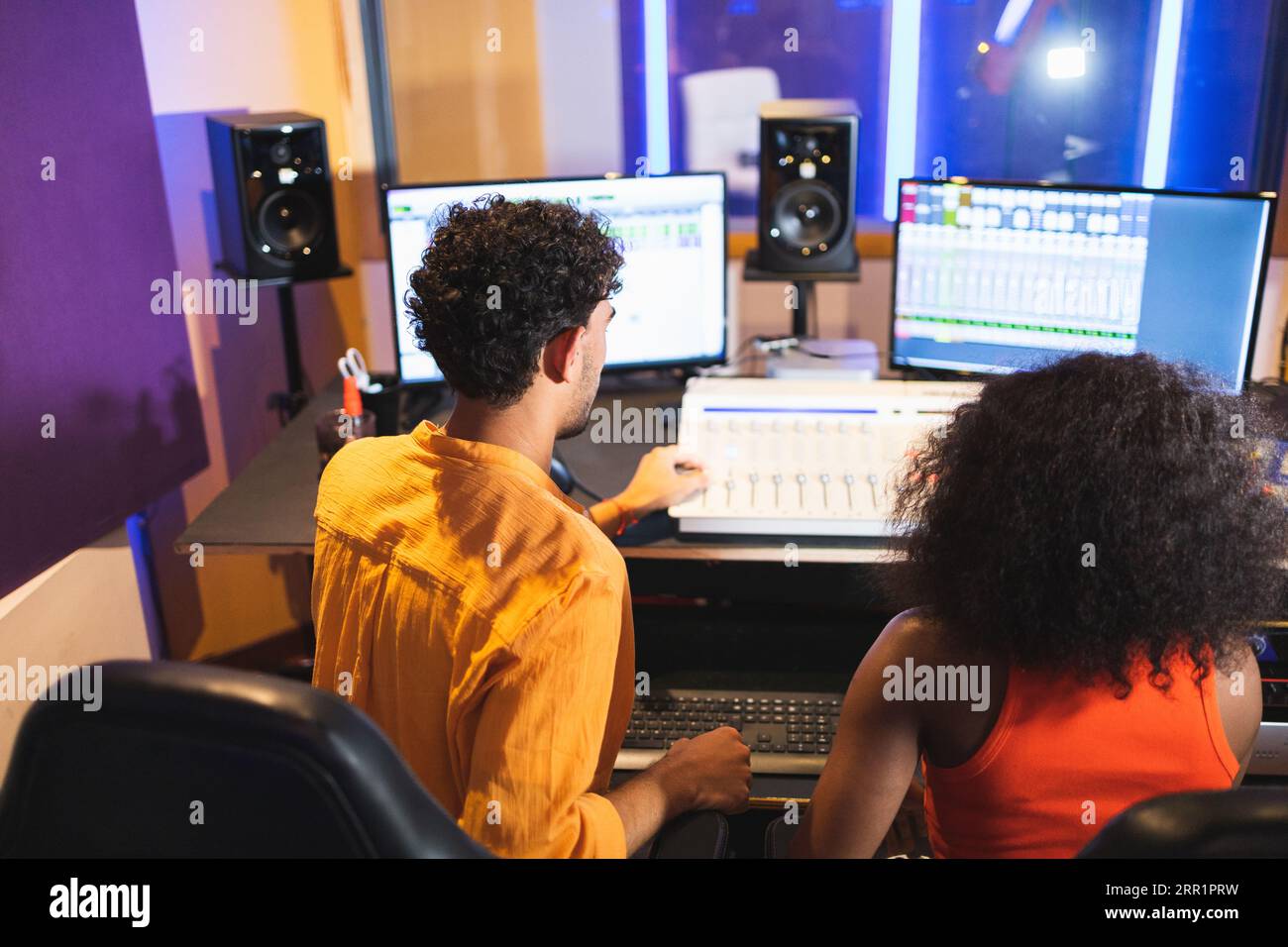 Von oben Rückansicht eines nicht erkennbaren männlichen Tontechnikers und einer afroamerikanischen Sängerin, die im Kontrollraum mit Computern aufgenommene Songs genießen Stockfoto