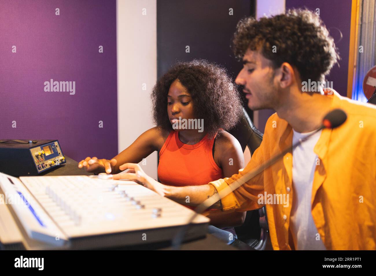 Männliche Toningenieurin und optimistische afroamerikanische Sängerin, die Hit-Songs kreiert, während sie Mischpulte und Computersoftware im Musikstudio verwendet Stockfoto