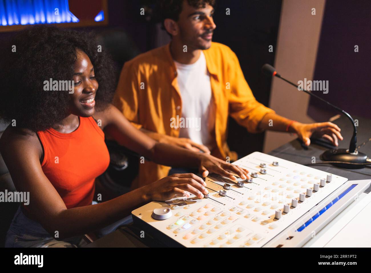 Männliche Toningenieurin und optimistische afroamerikanische Sängerin, die Hit-Songs kreiert, während sie Mischpulte und Computersoftware im Musikstudio verwendet Stockfoto
