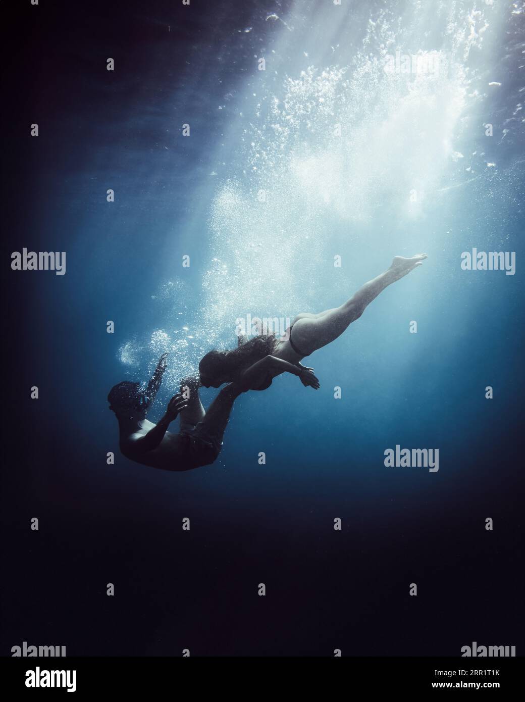 Seitenansicht eines nicht erkennbaren Paares in Schwimmkleidung, das die Hände hält, während es in Taucheranzug und Schnorchelmaske unter blauem Meer in der Nacht mit Hochspannung taucht Stockfoto