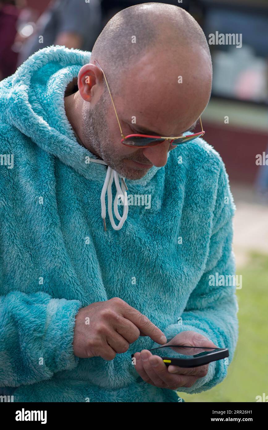 Junger Mann mit Sonnenbrille und flauschiger Jacke, der in sein Smartphone schreibt, Baden-Württemberg, Deutschland Stockfoto