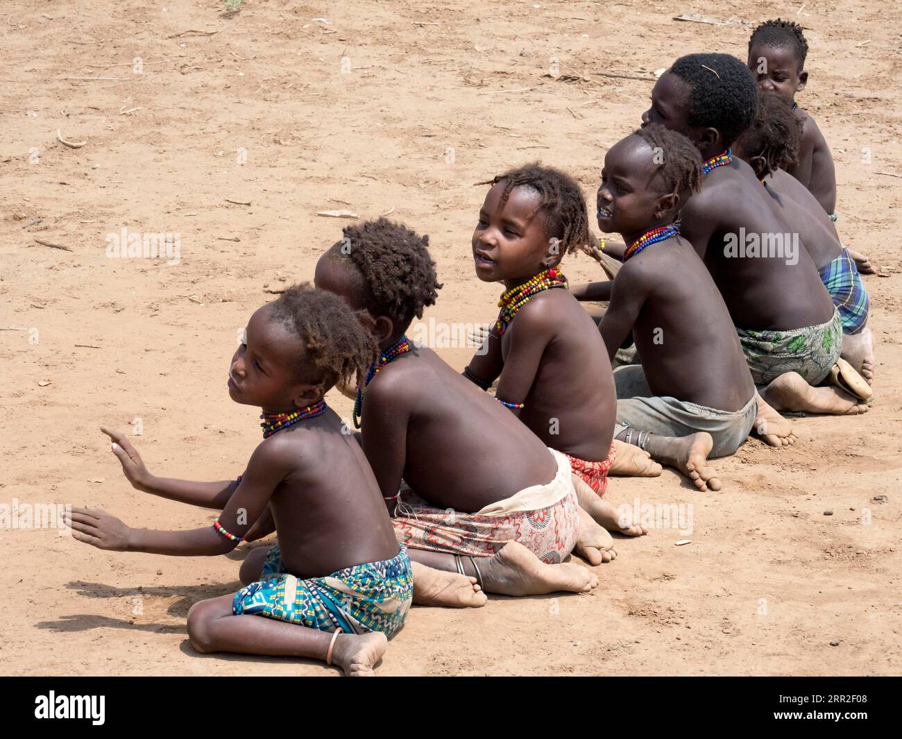 Singende glückliche Kinder sitzen auf sandigem Boden, Dassanech-Stamm, Äthiopien Stockfoto
