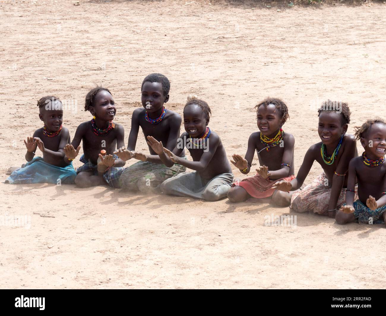 Singende glückliche Kinder sitzen auf sandigem Boden, Dassanech-Stamm, Äthiopien Stockfoto