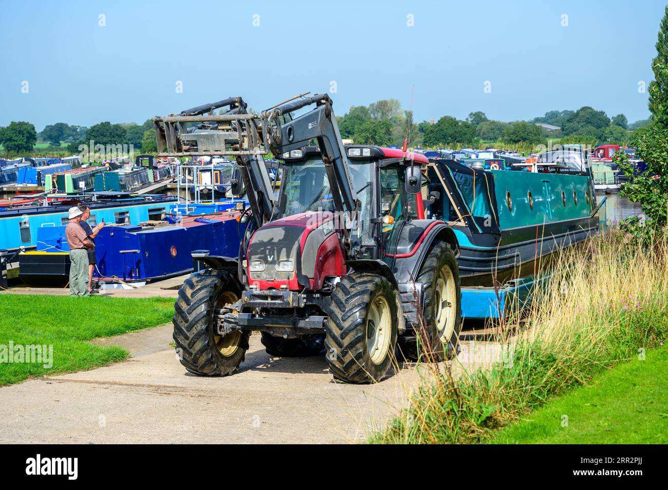 Ein Traktor und ein spezieller Anhänger werden verwendet, um ein Schmalboot über eine Hangbahn in einem Jachthafen aus dem Kanal zu ziehen. Stockfoto