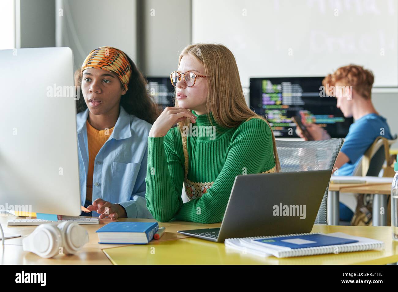 Schülerinnen, die mit Online-Präsentationen am Computer arbeiten, während sie im Klassenzimmer am Schreibtisch sitzen Stockfoto
