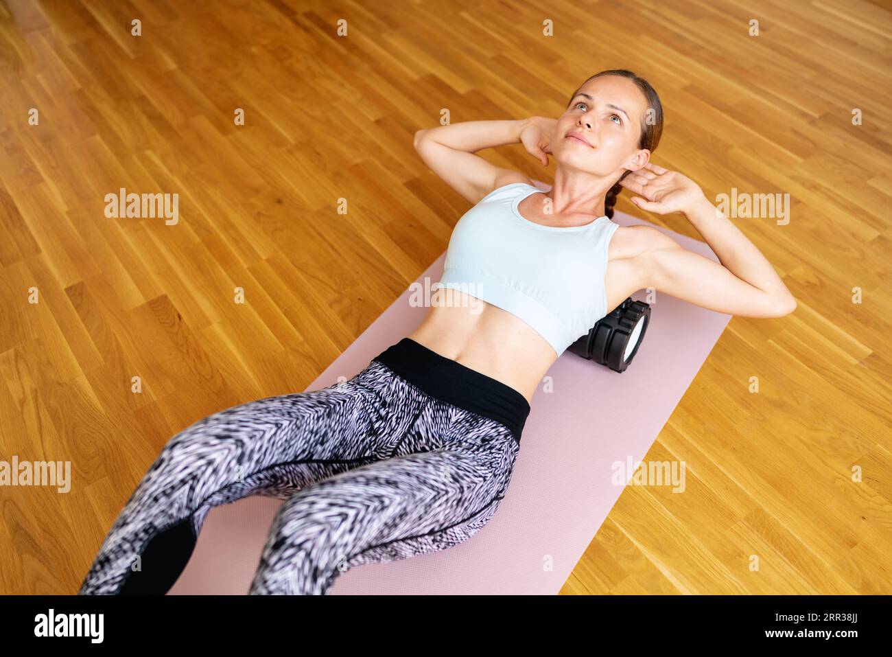 Sportliche Frau macht körperliche Bewegung auf Yogamatte mit Schaumstoffrolle, Selbstmuskelentlastung, Selbstmyofasziale Freisetzung. Stockfoto