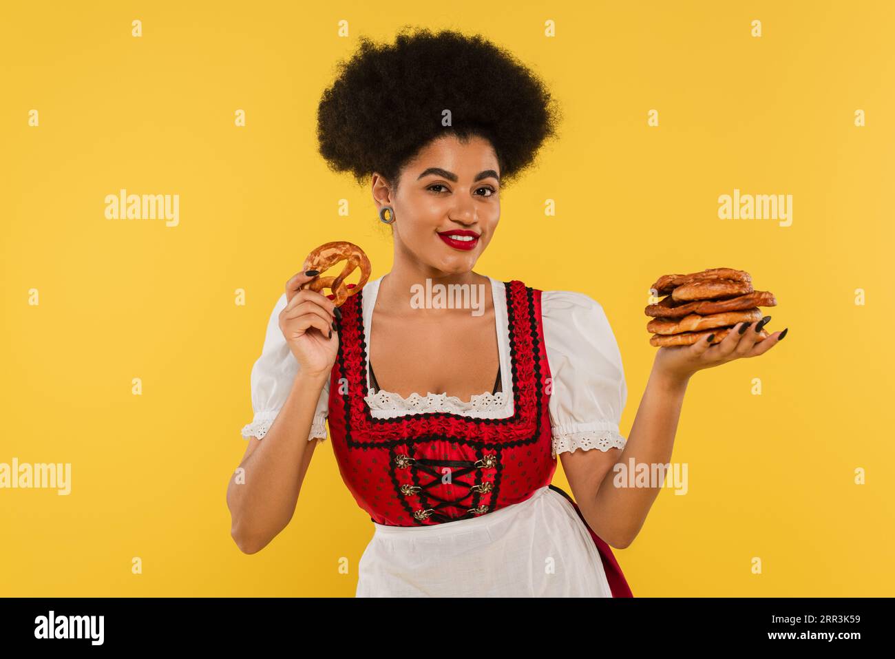 Fröhliche afroamerikanische Kellnerin im authentischen Kostüm, die Brezeln auf Gelb hält Stockfoto