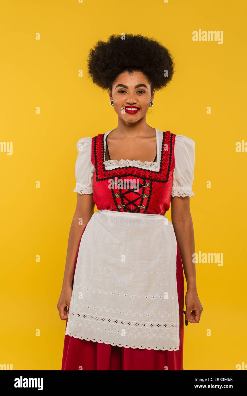 Freute afroamerikanische Kellnerin in authentischer bayerischer Tracht auf gelbem oktoberfest-Konzept Stockfoto