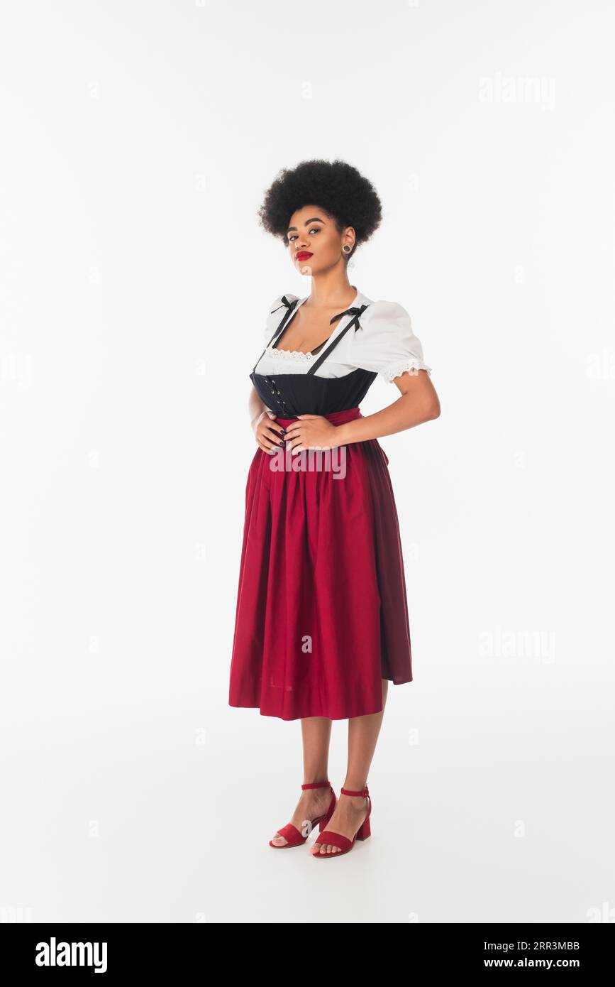 Selbstbewusste afroamerikanische oktoberfest-Kellnerin in traditioneller bayerischer Tracht, die auf weiß steht Stockfoto