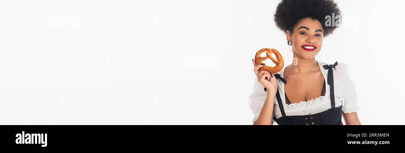 Fröhliche afroamerikanische oktoberfest-Kellnerin im Dirndl mit leckerer Brezel auf weißem Banner Stockfoto