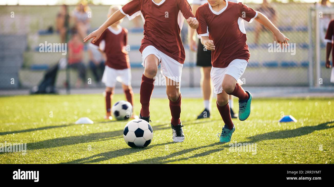 Happy Kids, die Fußball auf dem Schulhof üben. Junger Trainer mit Fußballspielern für Kinder im Training. Trainingssport für Jungen im sonnigen Sommer Stockfoto