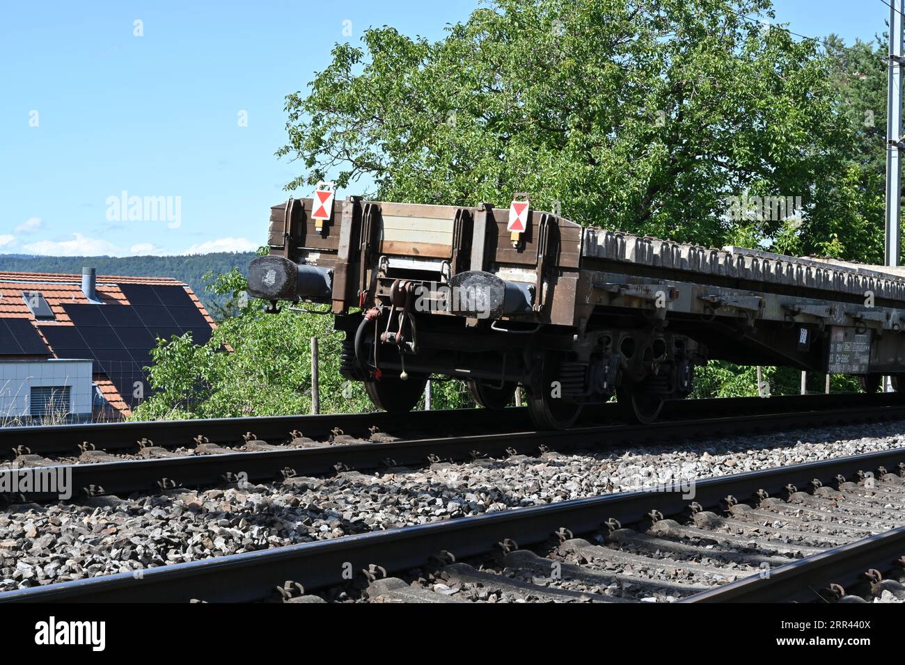 Auf den Schienen, die zum Schweizer Bahnhof Urdorf führen, steht ein Eisenbahnwagen mit mit Betonschwellen beladenen Zugstoßdämpfern. Stockfoto