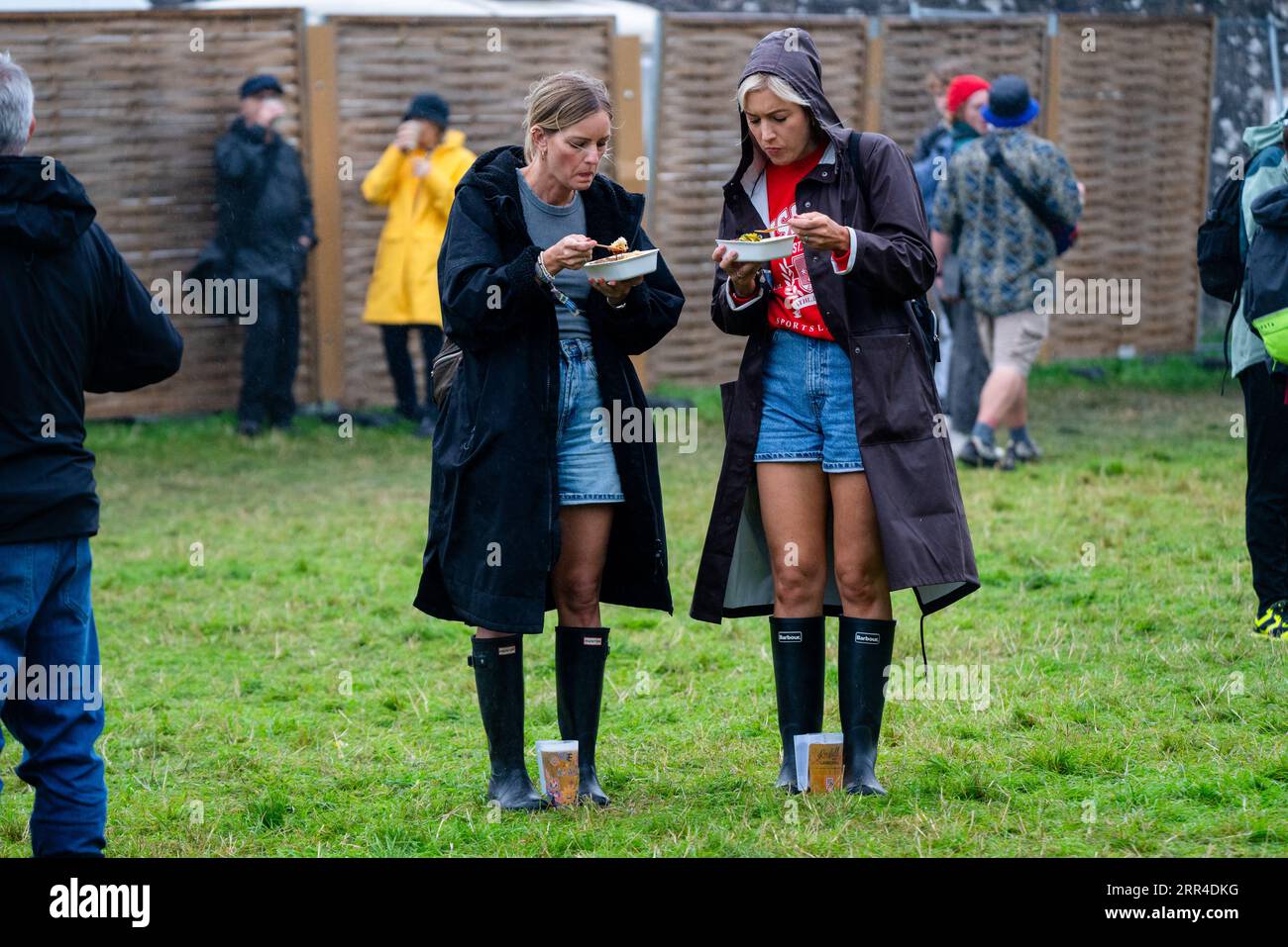 Zwei Frauen essen Fast Food von Tabletts im Regen und Schlamm. Green man Festival, Brecon, Wales, Großbritannien, 2023. Foto: Rob Watkins Stockfoto